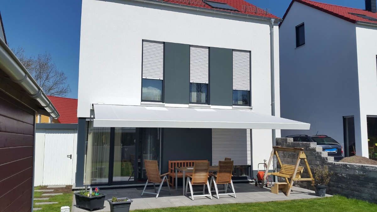 Ein weißes Haus mit einer Terrasse mit Tisch und Stühlen unter einer Markise.