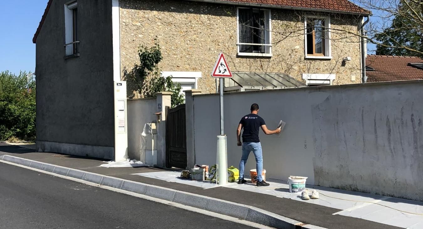 Un homme peint un mur à l'extérieur. Du matériel et un panneau de signalisation se trouvent à proximité.