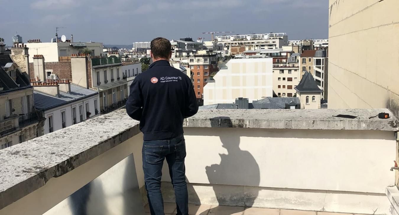 Un homme, juché sur un toit, contemple un paysage urbain par une journée ensoleillée.