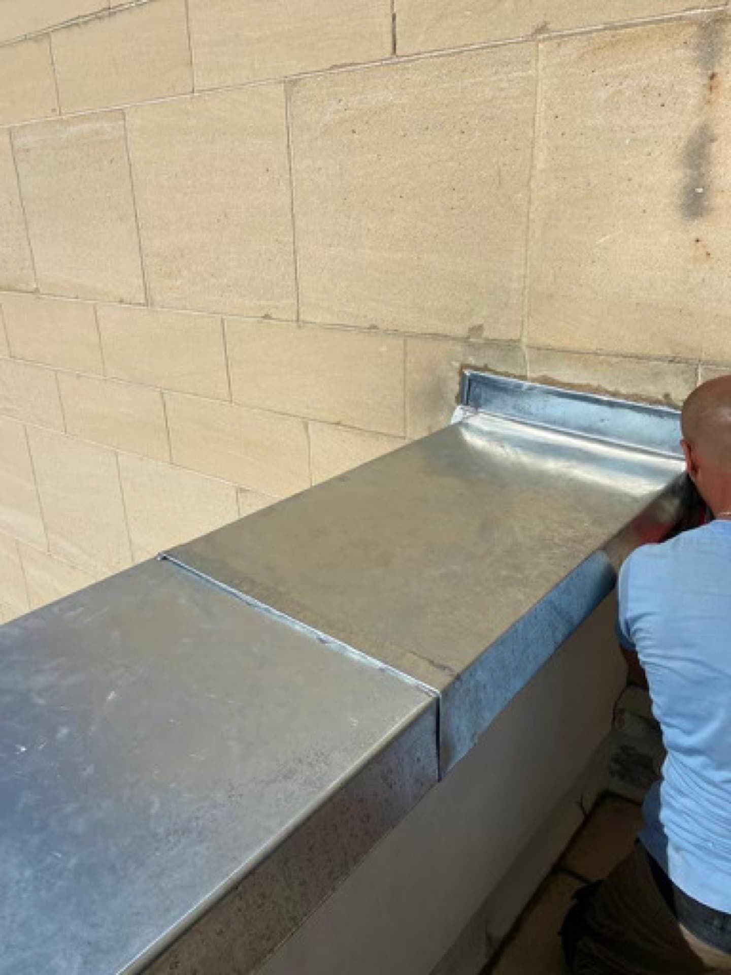 Une personne installe une bande de solin métallique sur un mur en pierre.