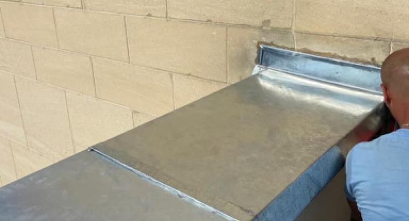 Personne travaillant sur une bande de solin métallique installée sur un mur de briques.