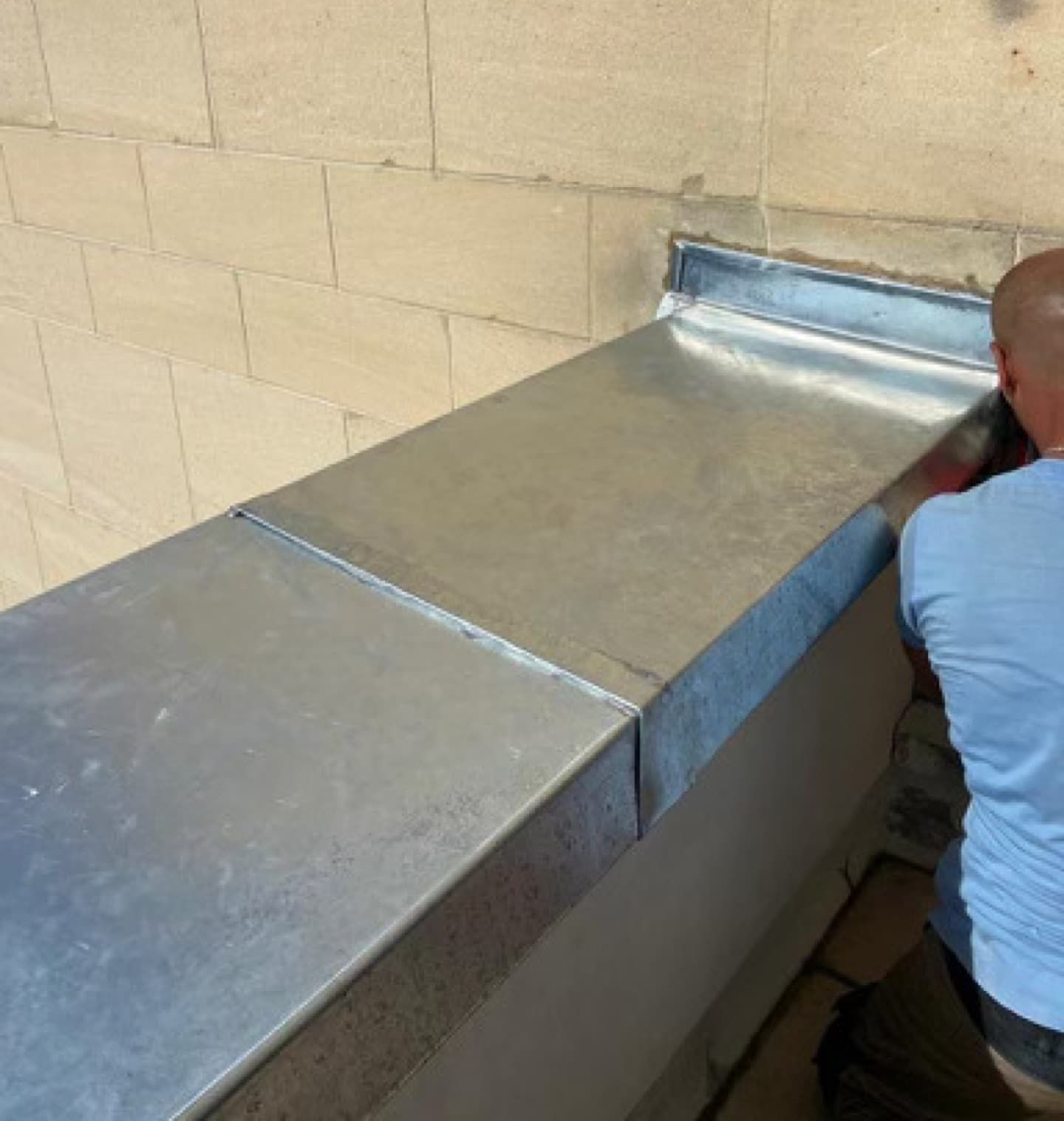 Un homme installe des solins métalliques sur un muret. Fond en briques.