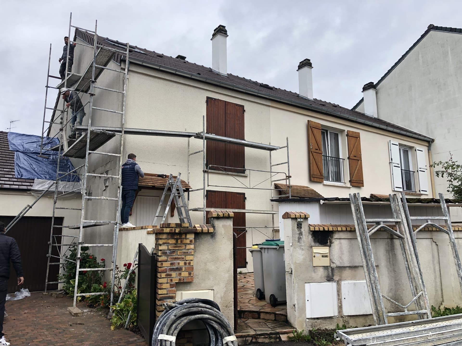 Maison en construction avec échafaudages ; personne sur une échelle ; journée nuageuse.