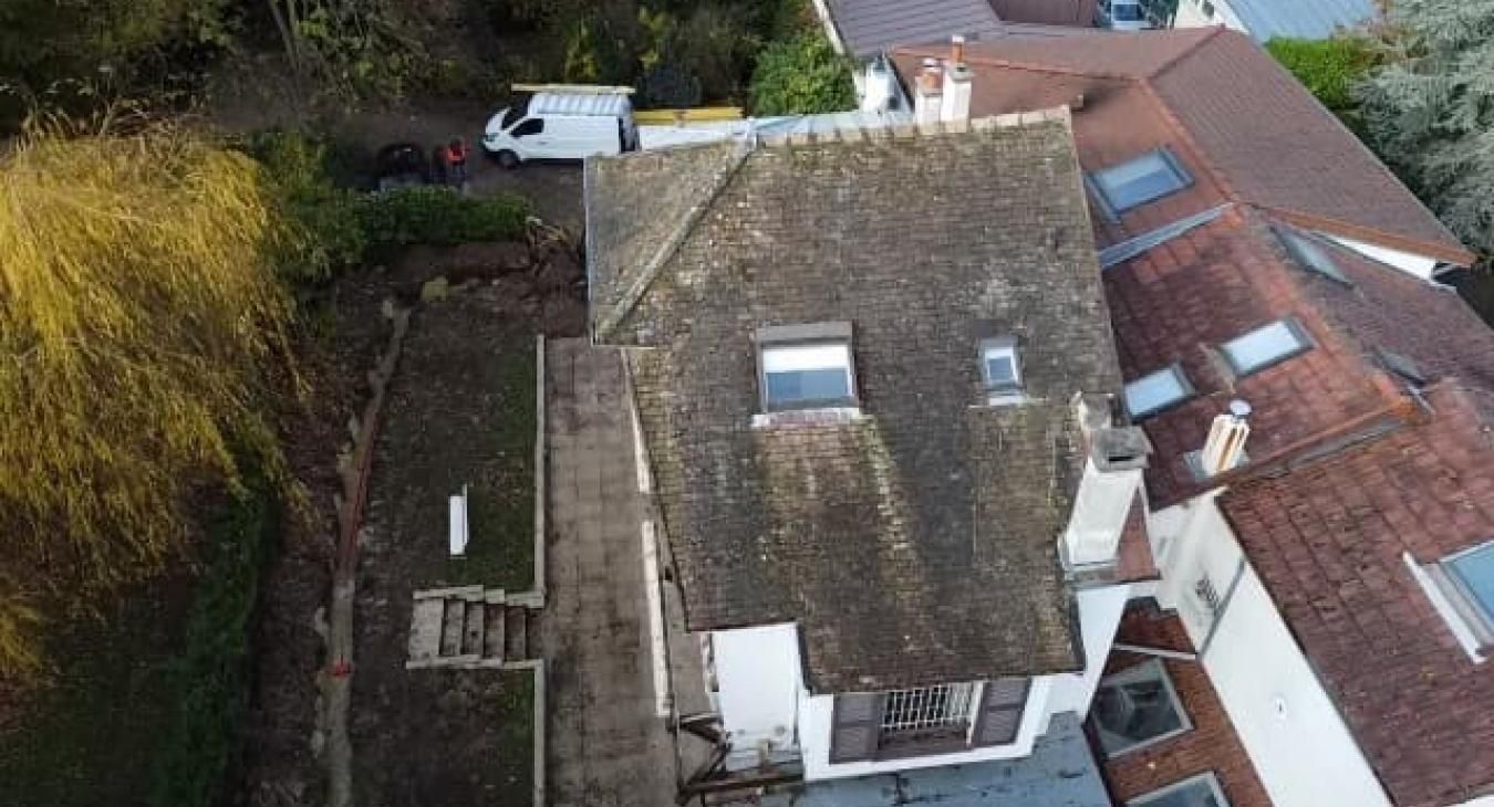 Vue aérienne d'une maison au toit gris et au bardage blanc ; une camionnette blanche est garée à proximité.