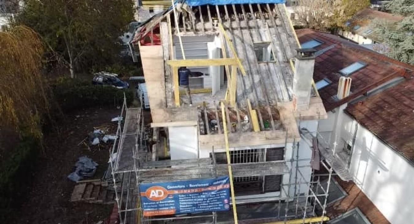 Maison en construction ; échafaudages, poutres de toit apparentes et banderole.