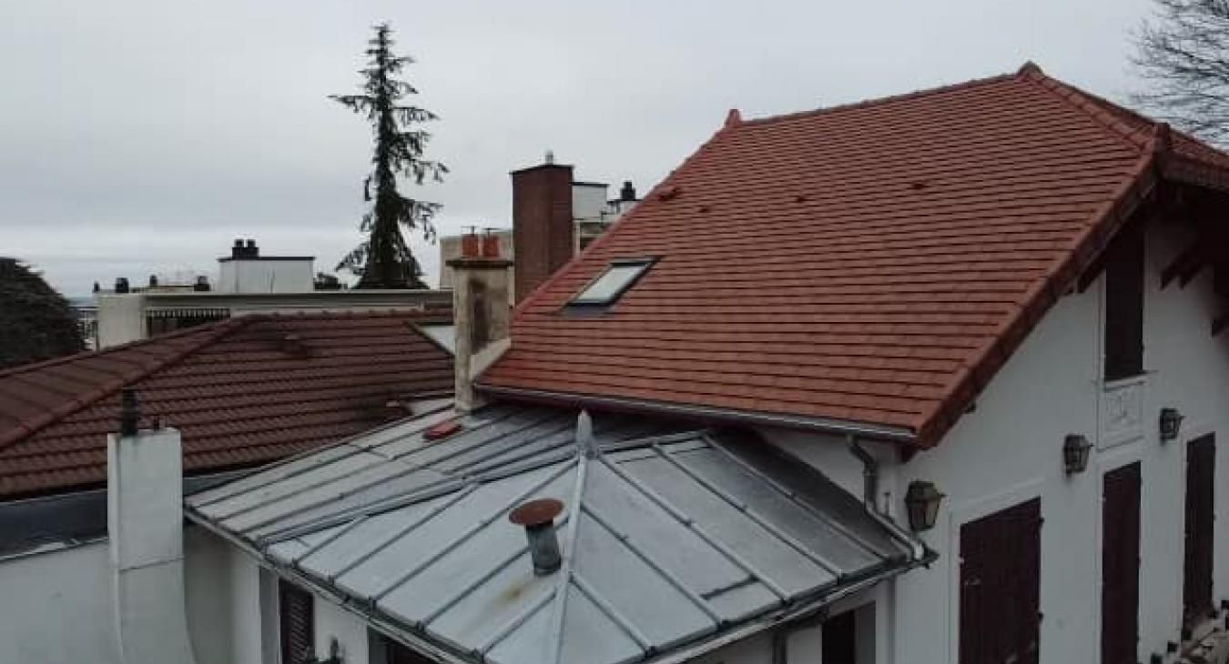 Maison blanche au toit de tuiles rouges, avec une extension en métal, sous un ciel nuageux.
