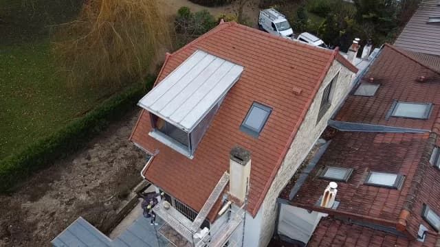 Toiture de tuiles rouges d'une maison avec lucarne métallique et puits de lumière ; vue aérienne.