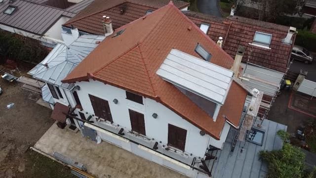 Maison au toit de tuiles rouges, aux murs blancs et aux volets bruns. Rénovation extérieure en cours.