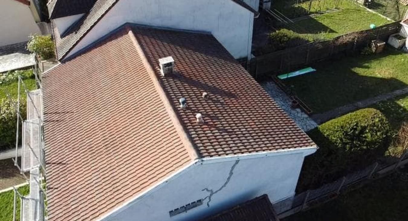 Vue aérienne d'une maison avec un toit de tuiles brunes, une cheminée et une petite pelouse verte.