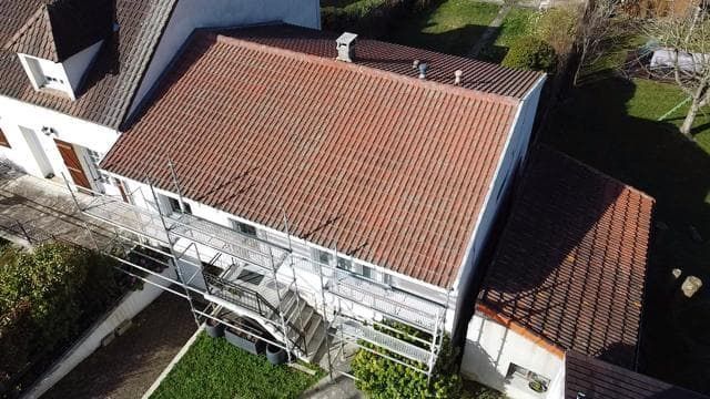 Vue aérienne d'un bâtiment au toit de tuiles rouges, avec des échafaudages sur le côté.