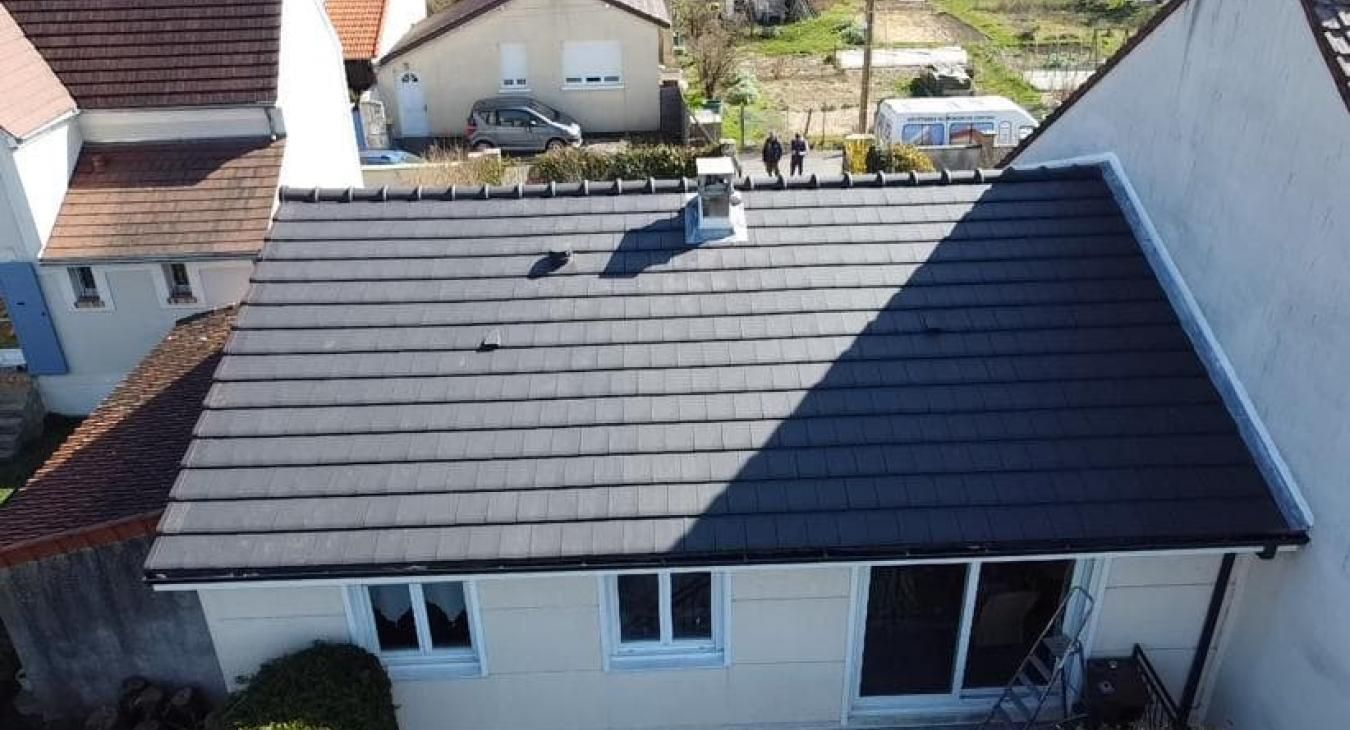 Une maison avec un toit en tuiles gris foncé neuves, une cheminée et des maisons environnantes.