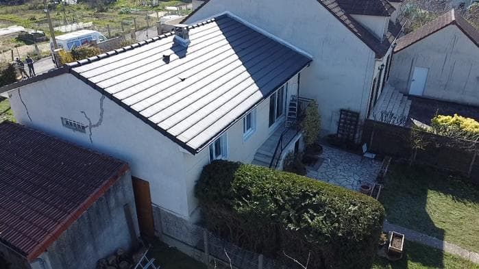 Une maison au toit gris foncé et aux murs blancs. Il y a un jardin verdoyant.