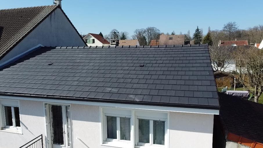 Vue en contre-plongée d'une maison au toit de tuiles gris foncé par une journée ensoleillée.