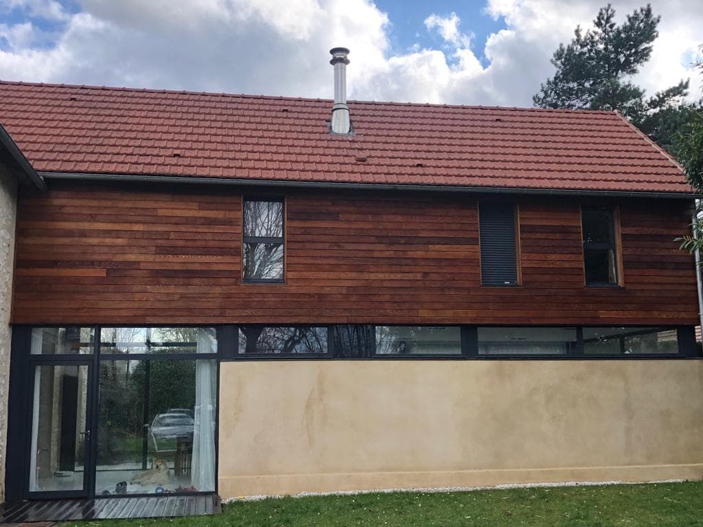 Extérieur d'un bâtiment de deux étages avec un toit de tuiles rouges et un bardage en bois.