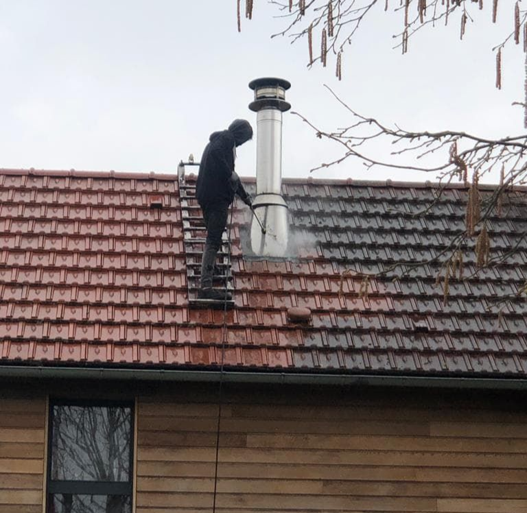 Une personne nettoie un toit de tuiles au nettoyeur à haute pression.