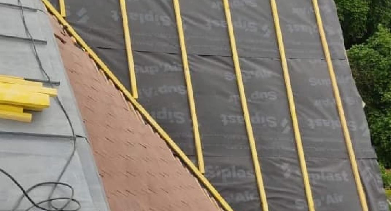 Toiture en cours de réalisation, montrant la sous-couche noire, les liteaux jaunes et la première rangée de bardeaux de bois.