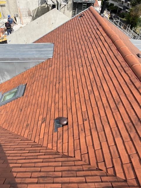 Toit en tuiles rouges avec une ventilation et un puits de lumière ; un chantier de construction est visible en arrière-plan.