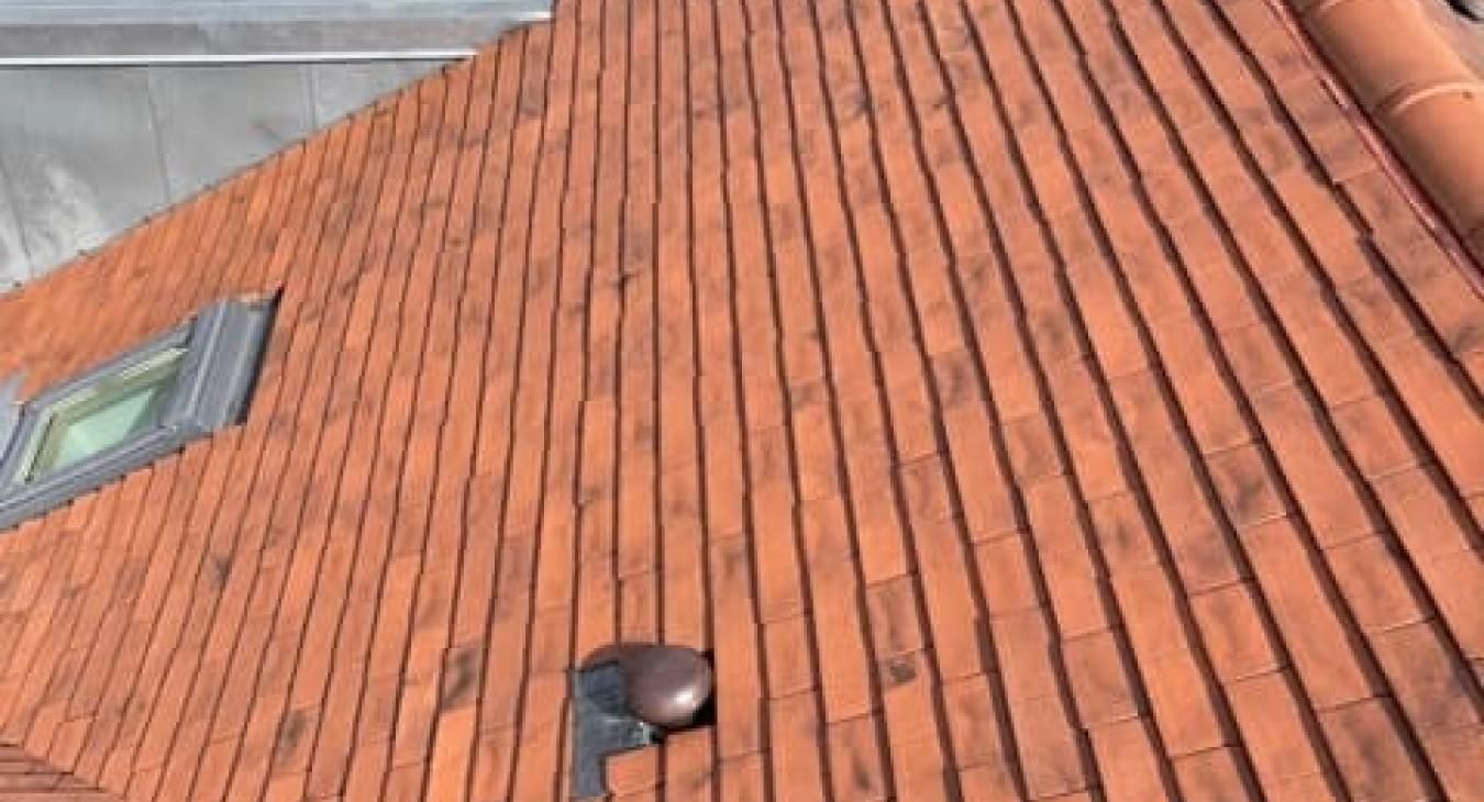 Toit en tuiles orange avec une fenêtre et un conduit de ventilation.