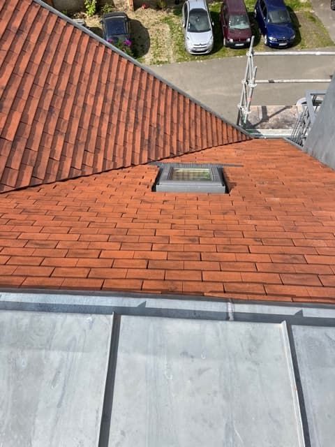 Toit en tuiles rouges avec puits de lumière et solins en plomb, donnant sur des voitures stationnées.