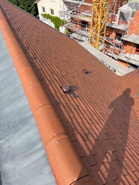 Toit en tuiles brunes avec des éléments métalliques, probablement sur un bâtiment, chantier de construction en arrière-plan.