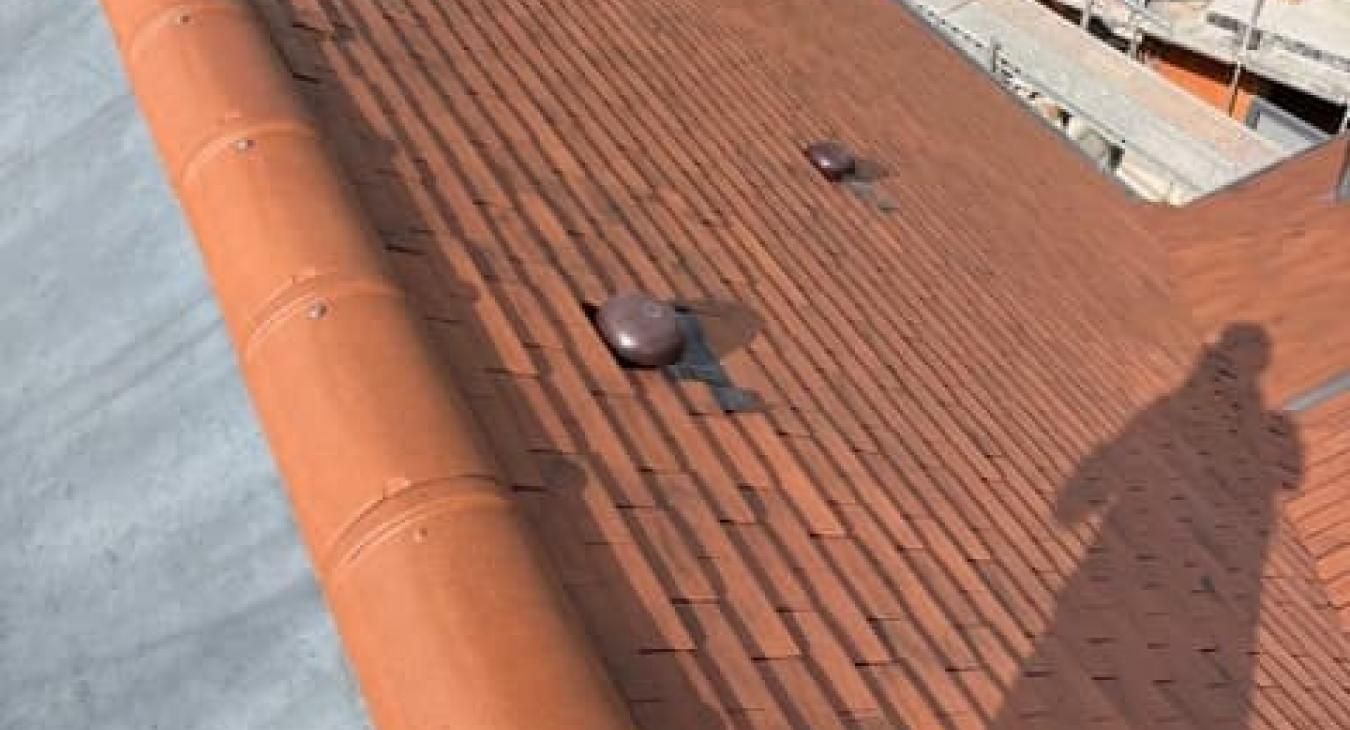 Toit en tuiles de terre cuite avec deux aérations brun foncé et une gouttière, vu de dessus.