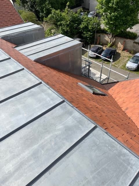Vue d'un toit avec des panneaux métalliques gris et des tuiles en terre cuite rouge.