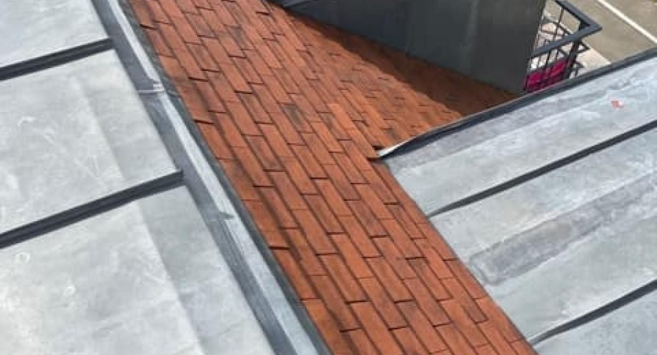 Gros plan sur un toit avec une partie en briques et une couverture métallique, dans des tons de rouge, de gris et de noir.