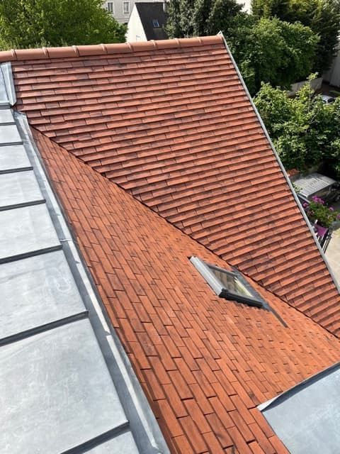 Un toit de tuiles rouges avec une partie de toit plate en métal gris et un petit puits de lumière.