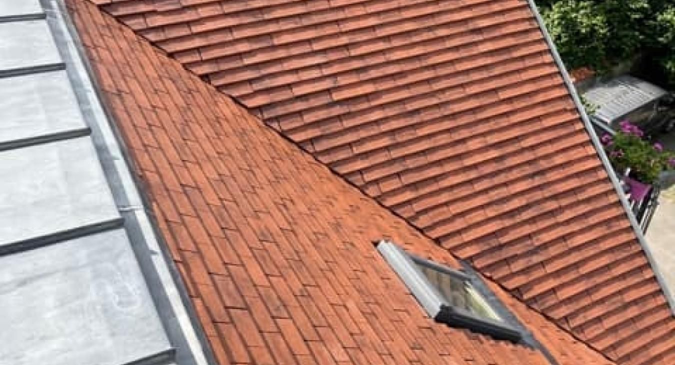 Toiture en tuiles rouges avec un puits de lumière jouxtant une section de toiture métallique.