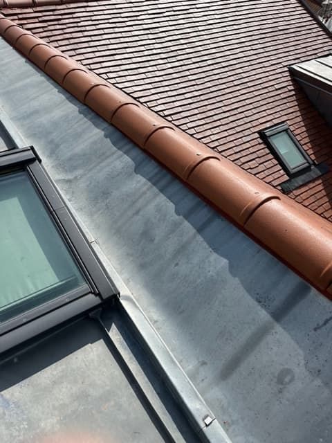 Toiture en tuiles rouges avec solin métallique, laissant apparaître deux lucarnes.