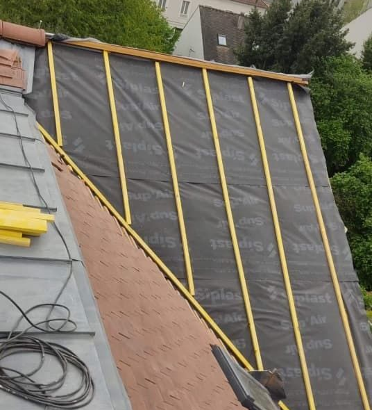 Toiture en construction avec sous-couche noire, liteaux jaunes et quelques tuiles existantes.