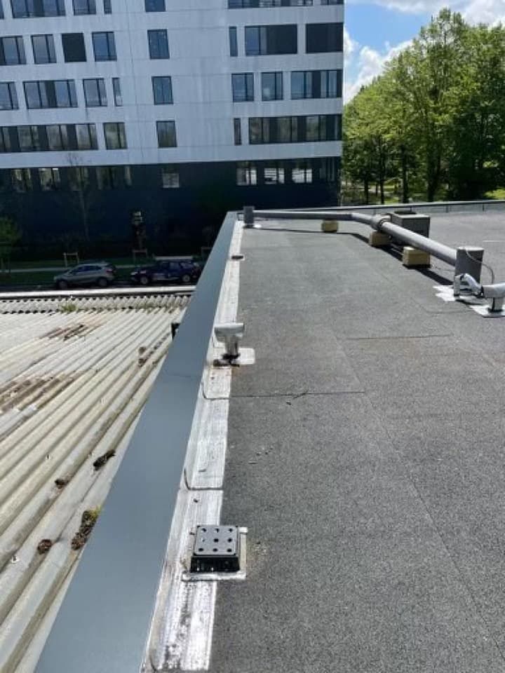 Un toit plat et noir avec une rambarde métallique, à côté d'un toit en tôle ondulée.