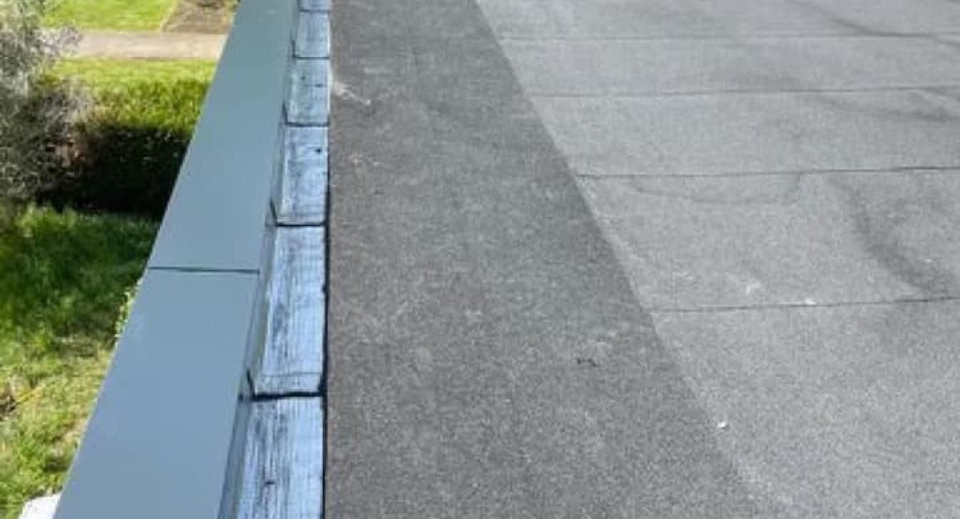 Toit plat recouvert de bardeaux d'asphalte foncés, avec des garnitures en bois et un liseré gris.