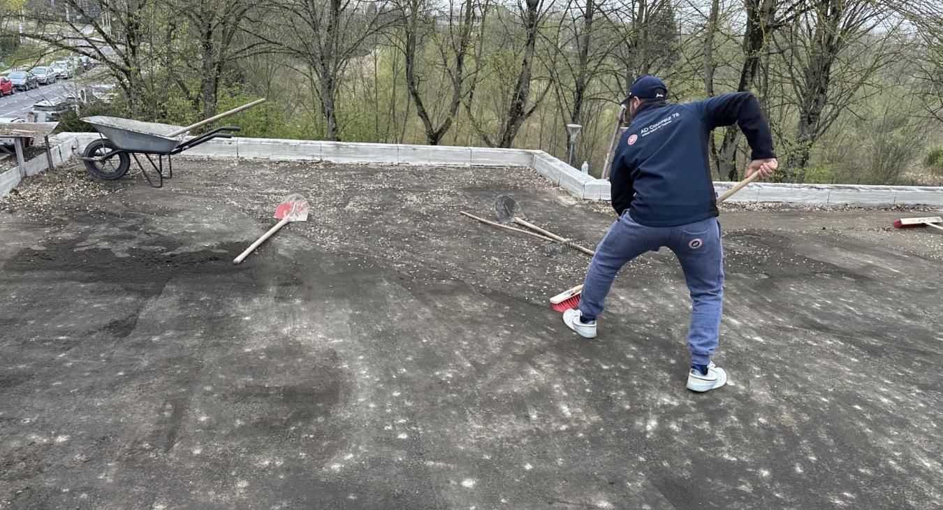 Une personne travaille sur un toit, donnant des coups de pied, entourée d'outils et d'une brouette.