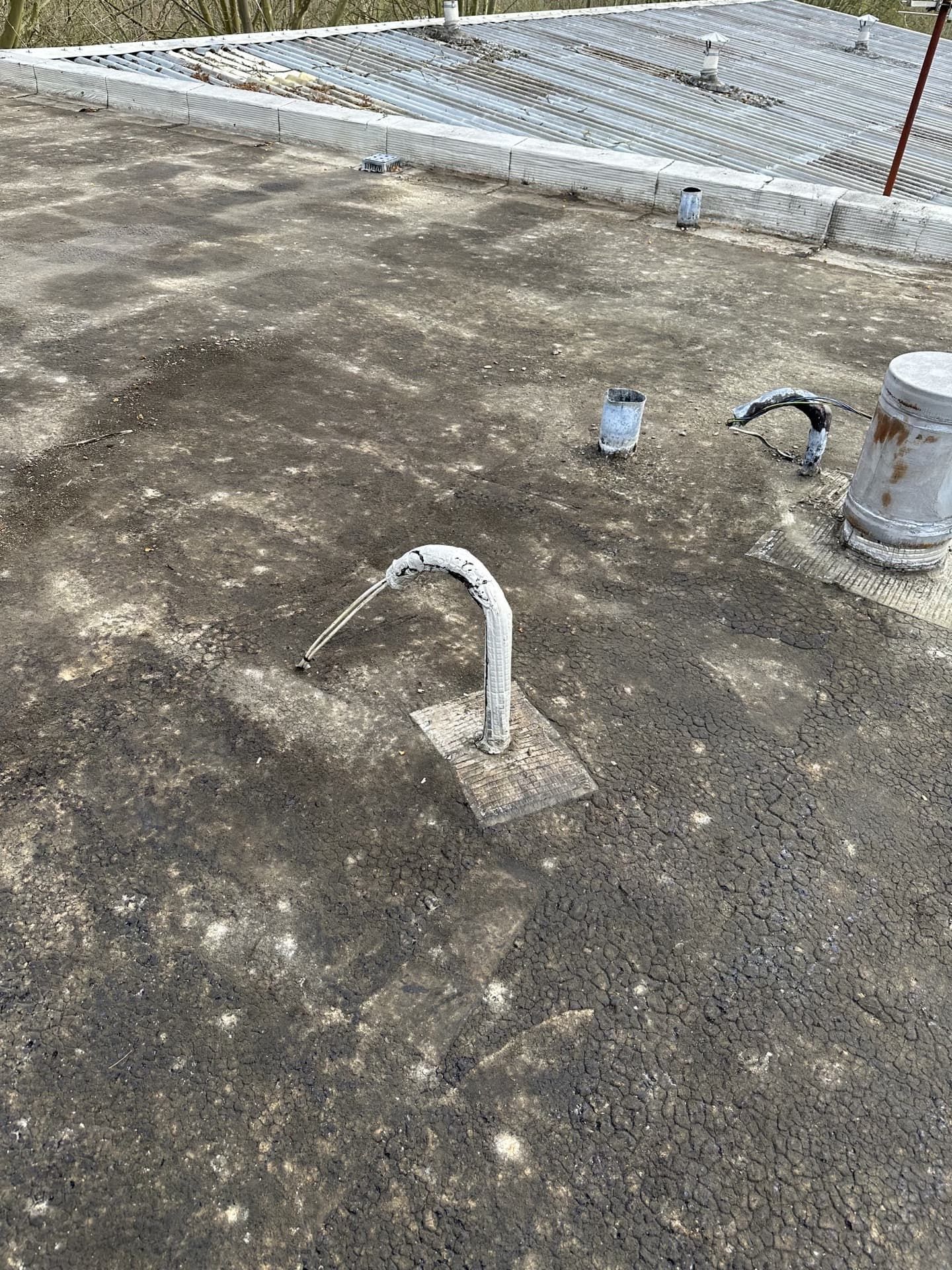 Une scène sur un toit avec de l'asphalte gris et des tuyaux de ventilation métalliques.