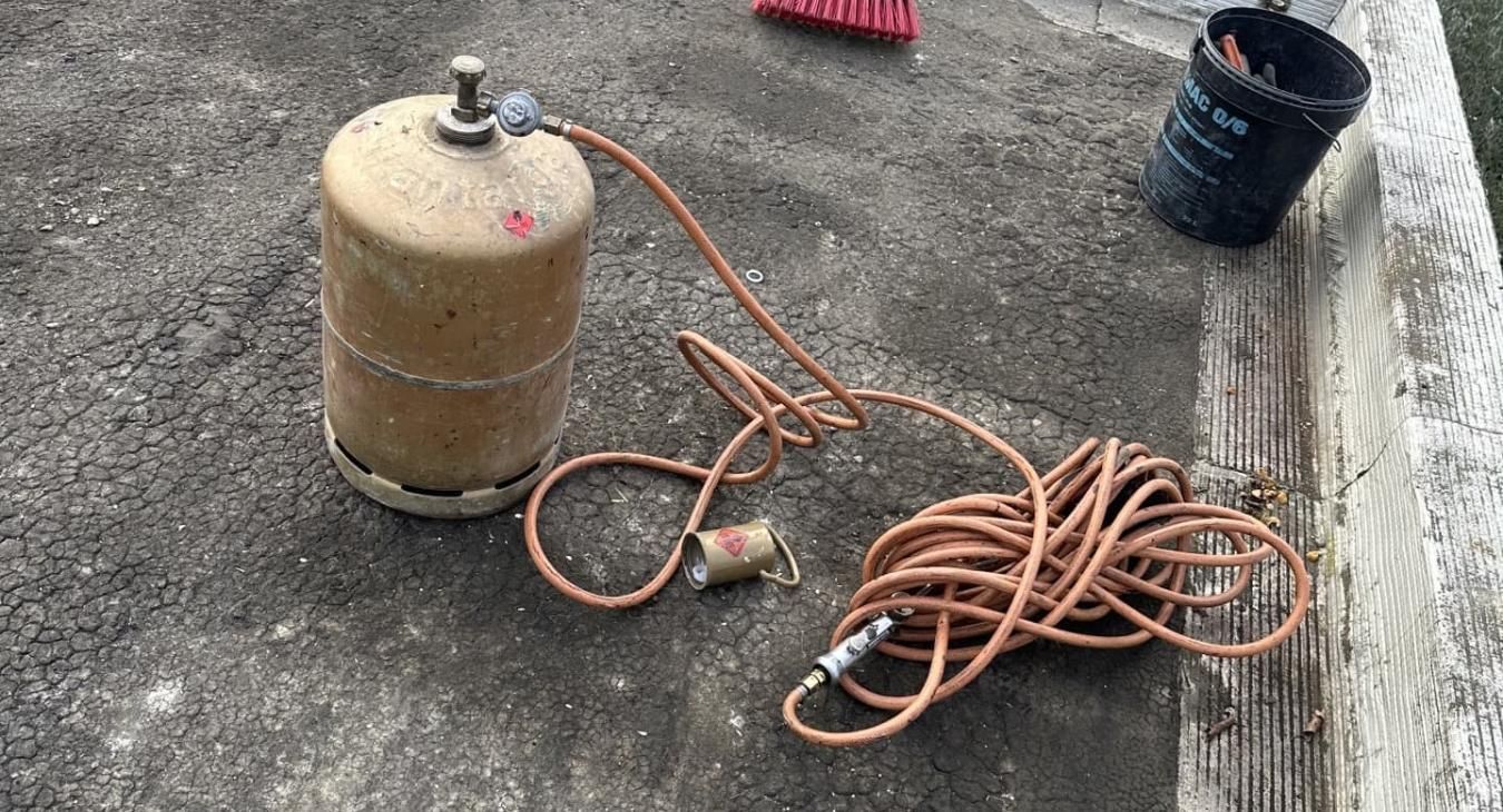 Réservoir de propane avec tuyauterie en cuivre et tête de torche posé sur une surface en béton.