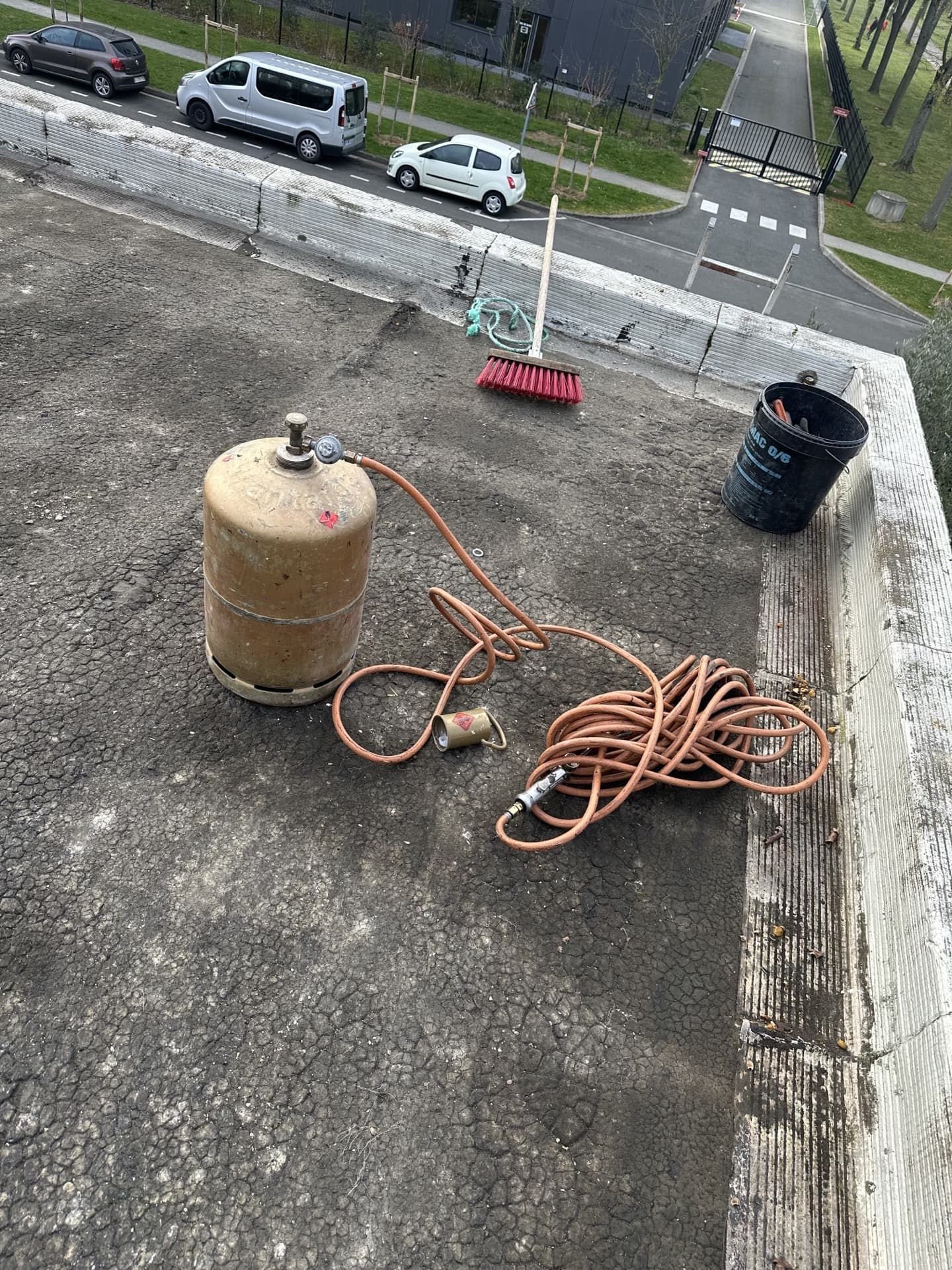 Scène sur un toit avec une bonbonne de propane, un tuyau d'arrosage, un seau et un balai.
