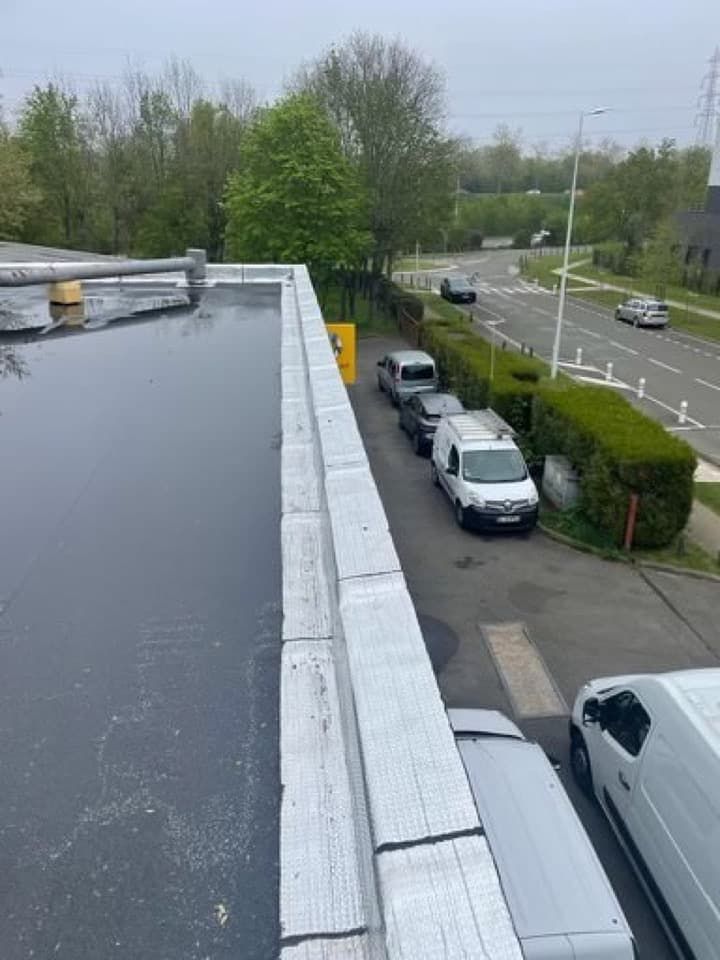 Vue depuis un toit plat, donnant sur des voitures garées le long d'une route bordée de haies et d'arbres taillés.