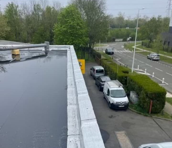 Vue depuis un toit plat et sombre sur une route où circulent des voitures.