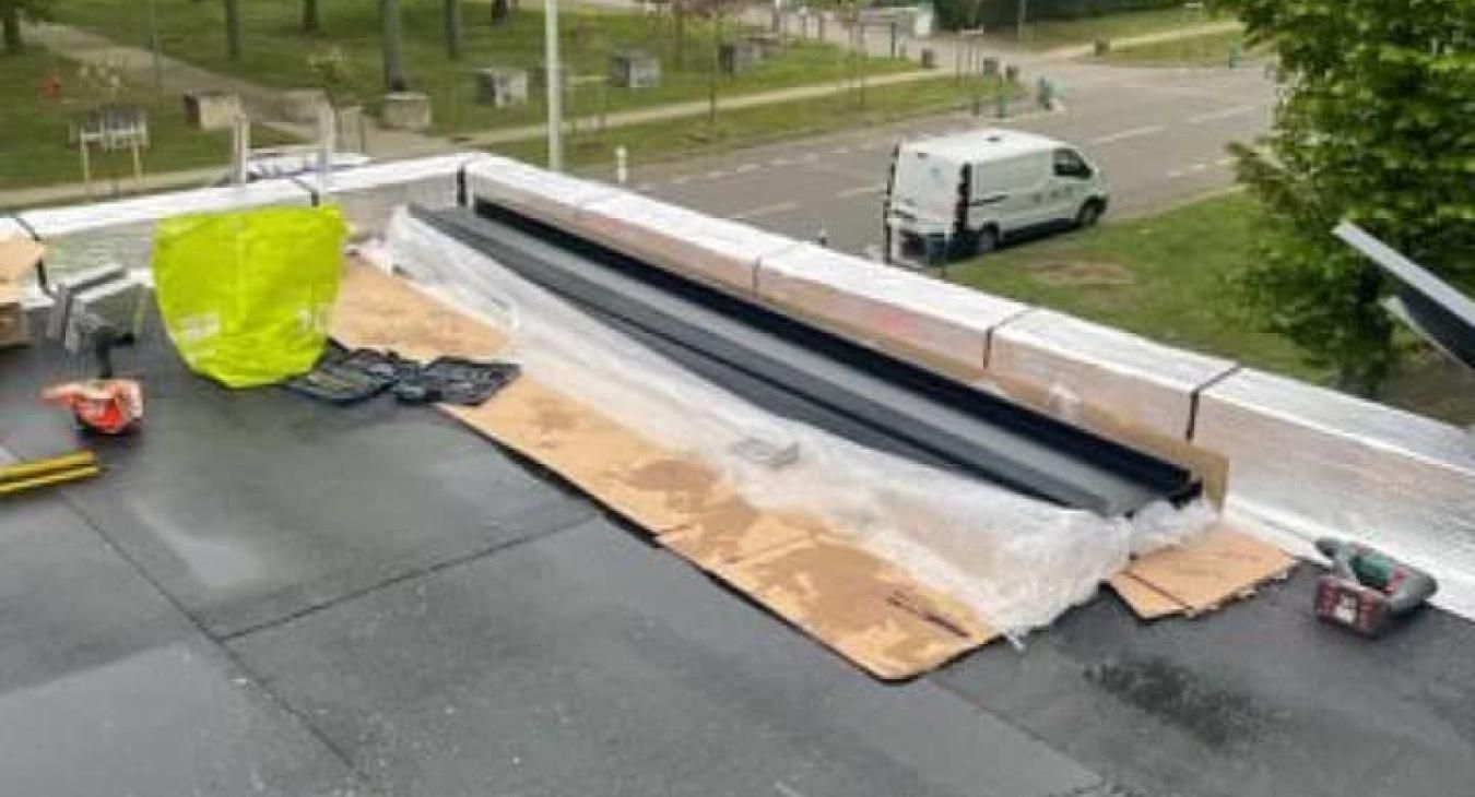 Toit plat avec des matériaux de construction et une camionnette de chantier garée à proximité.