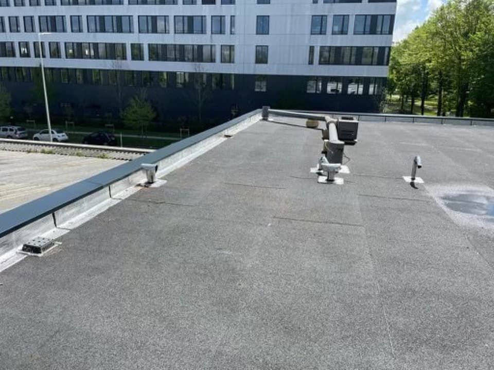 Toit plat noir à usage commercial, avec des aérations et un bâtiment en arrière-plan.