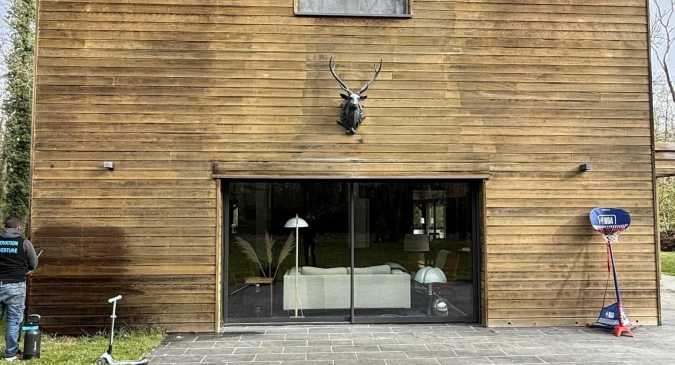 Maison en bois à l'extérieur, avec de grandes portes vitrées dévoilant un intérieur moderne.