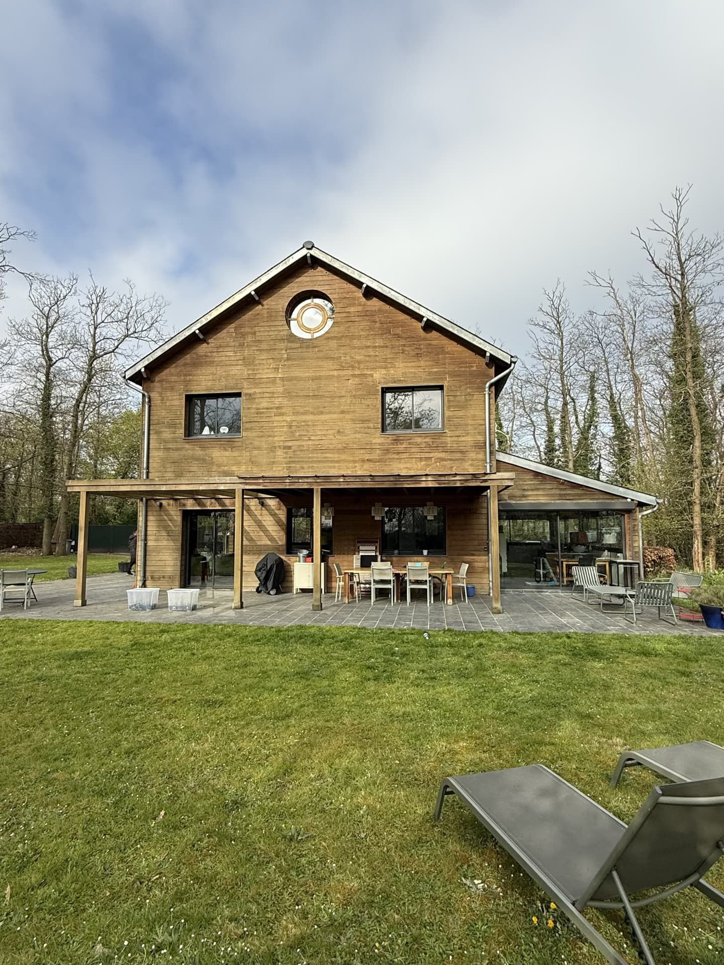 Maison en bois de deux étages avec terrasse, située sur une pelouse.
