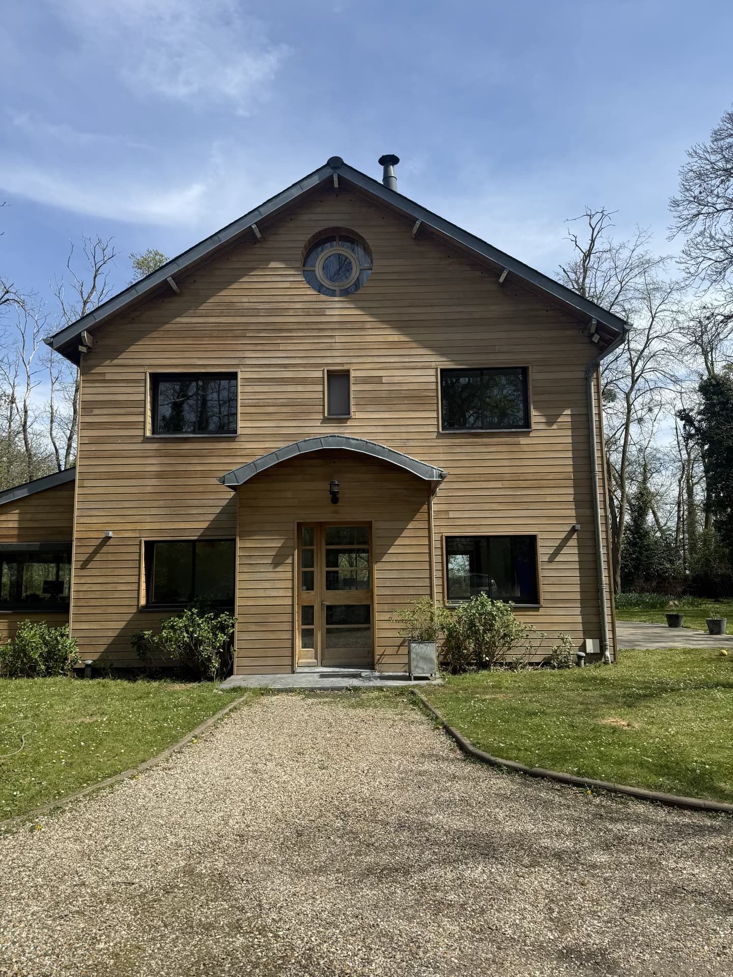 Maison en bois avec allée de gravier, entourée de verdure.
