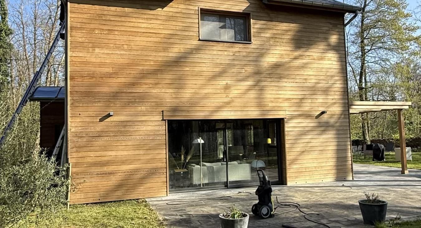 Maison avec bardage en bois brun et grandes portes vitrées, terrasse extérieure avec nettoyeur à haute pression.
