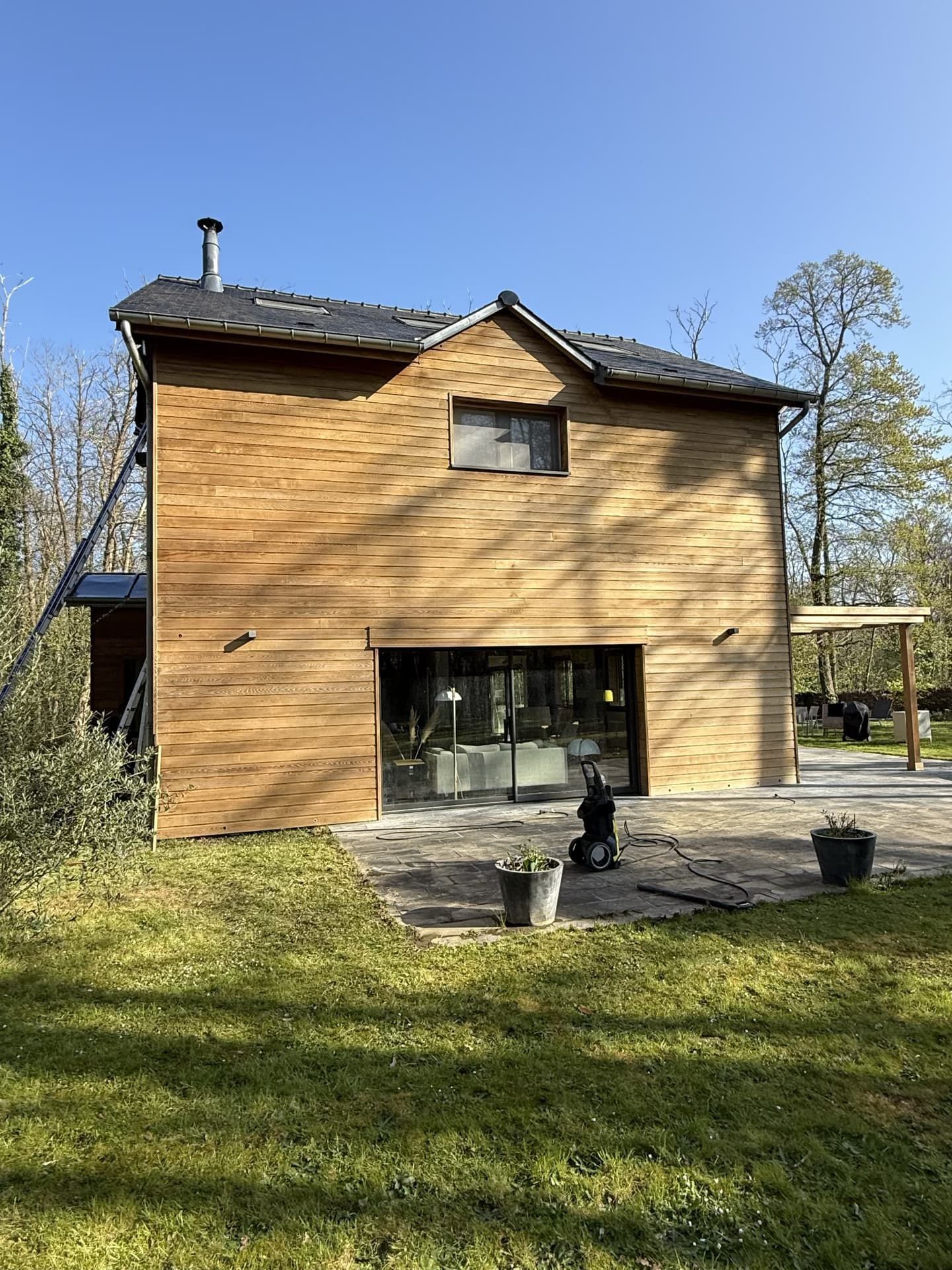 Maison moderne avec bardage en bois, portes vitrées et patio.