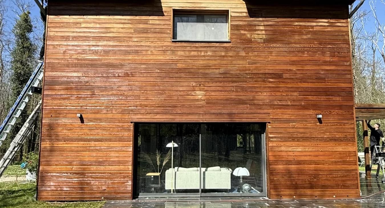 Maison en bois avec de grandes portes vitrées, une petite fenêtre et deux appliques murales.