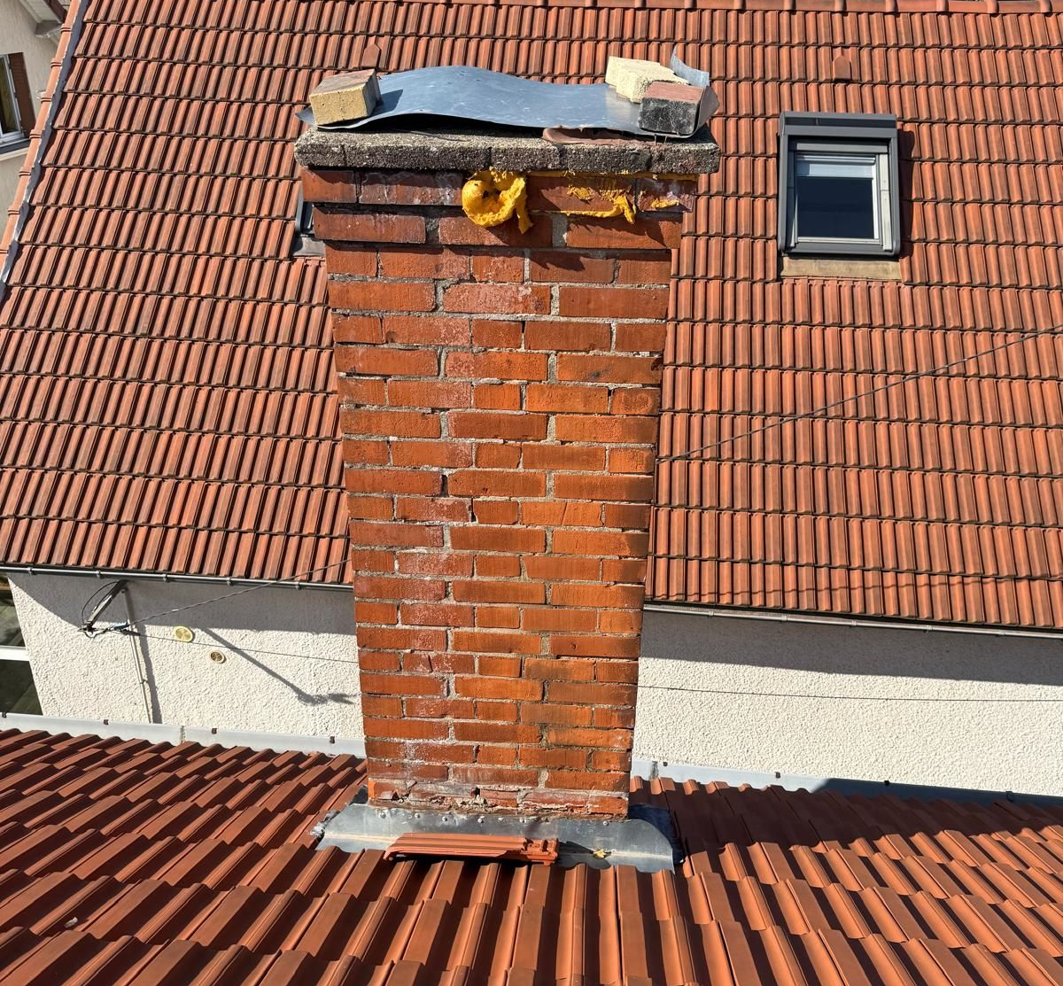 Cheminée en briques sur un toit de tuiles rouges, avec une petite lucarne.