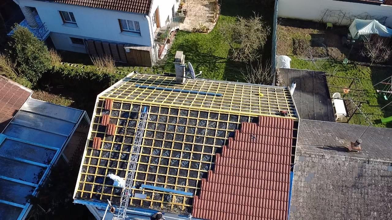 Vue aérienne d'un toit de maison partiellement recouvert de tuiles brunes, laissant apparaître la charpente en bois.