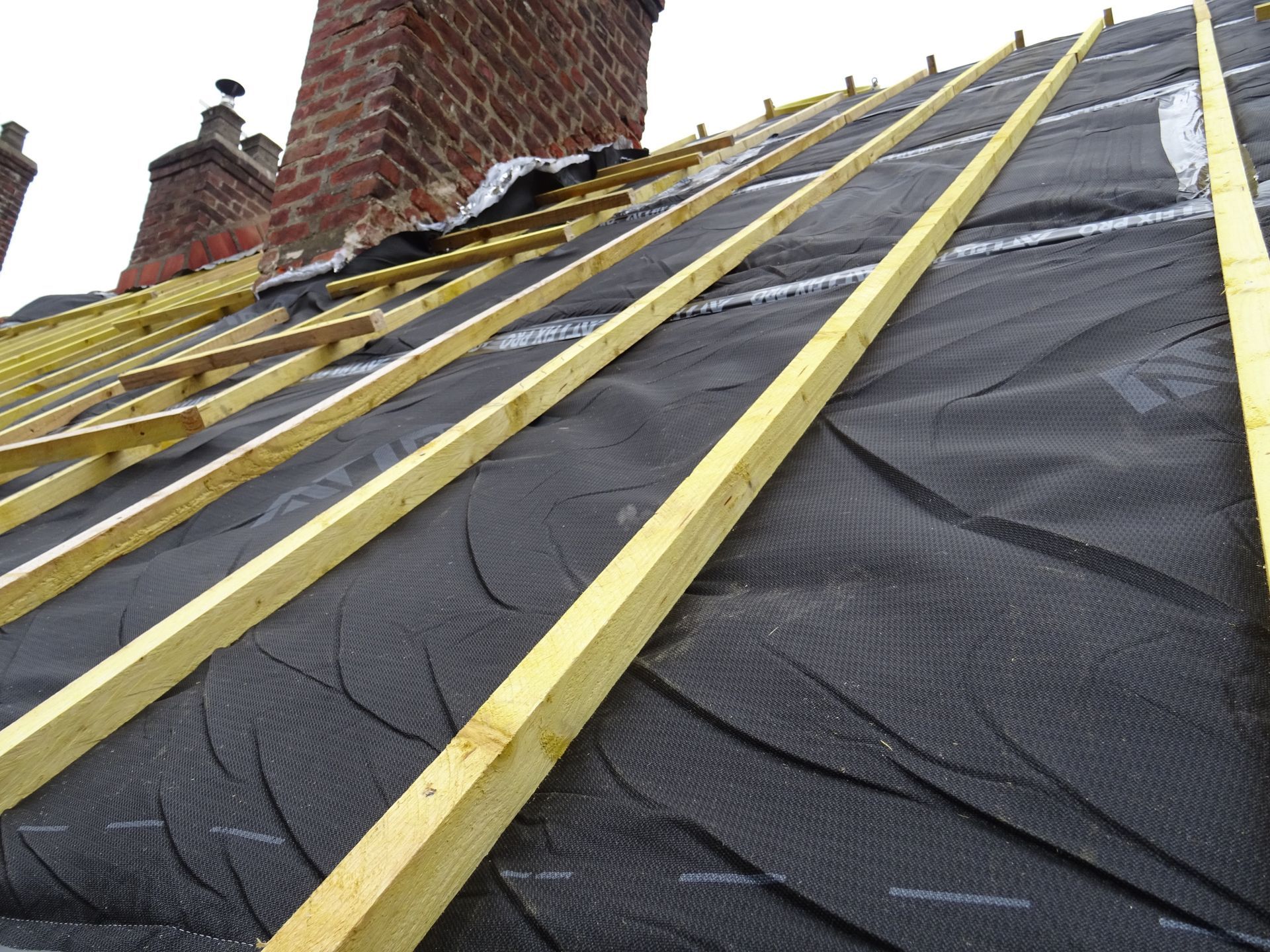 Toiture en construction : sous-couche noire, poutres en bois, cheminée en briques.